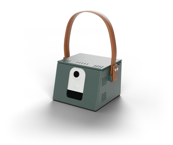 The TahtX box: dark green body, a camera behind the window in the sloped front, and a tan leather carrying strap on top.
